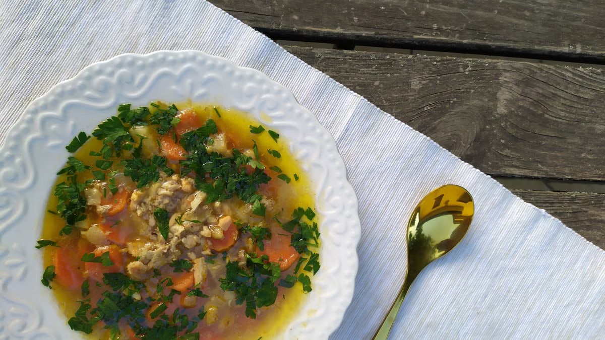Delicious homemade chicken soup garnished with fresh parsley, served on a rustic table setting.